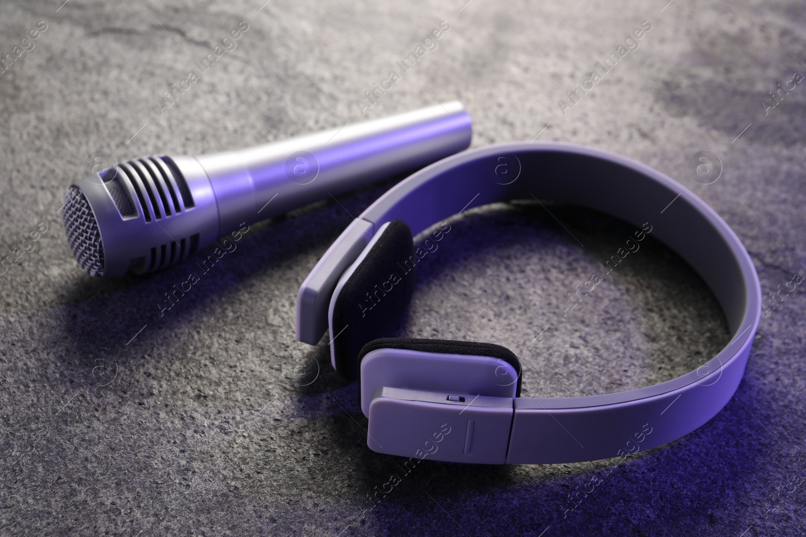 Photo of Microphone and headphones on grey textured table, closeup. Sound recording and reinforcement