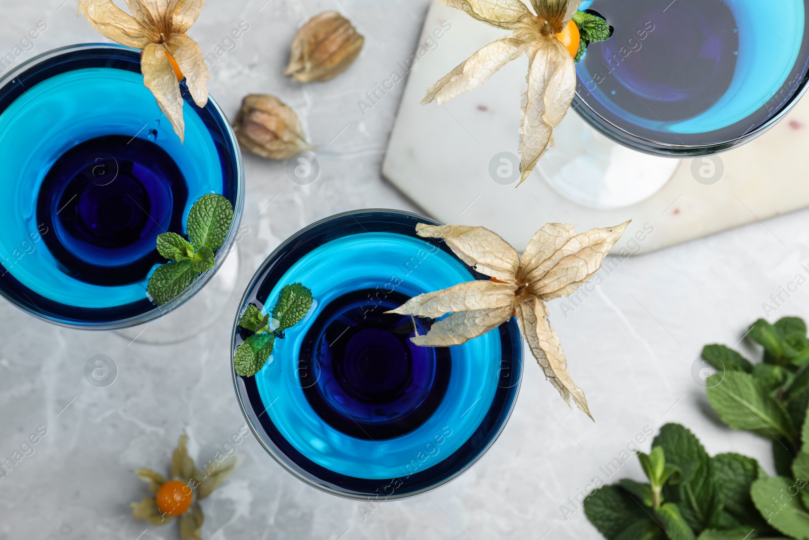 Photo of Tasty cocktail decorated with physalis fruits and mint on grey table, flat lay