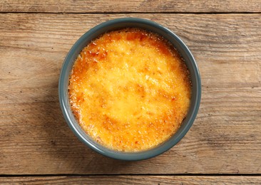 Photo of Delicious creme brulee in ceramic ramekin on wooden table, top view