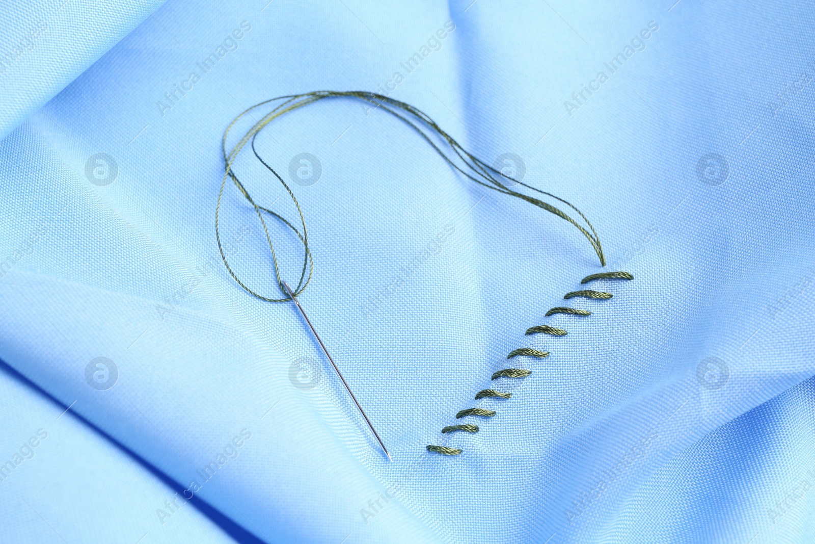 Photo of Sewing needle with thread and stitches on light blue cloth, top view