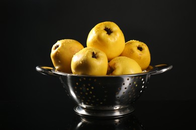 Tasty ripe quinces with water drops in metal colander on black mirror surface