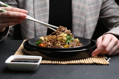 Photo of Stir-fry. Woman eating tasty noodles with meat and vegetables at dark textured table, closeup