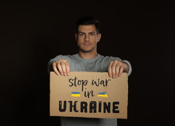 Image of Unhappy man holding sign with phrase Stop War in Ukraine on black background
