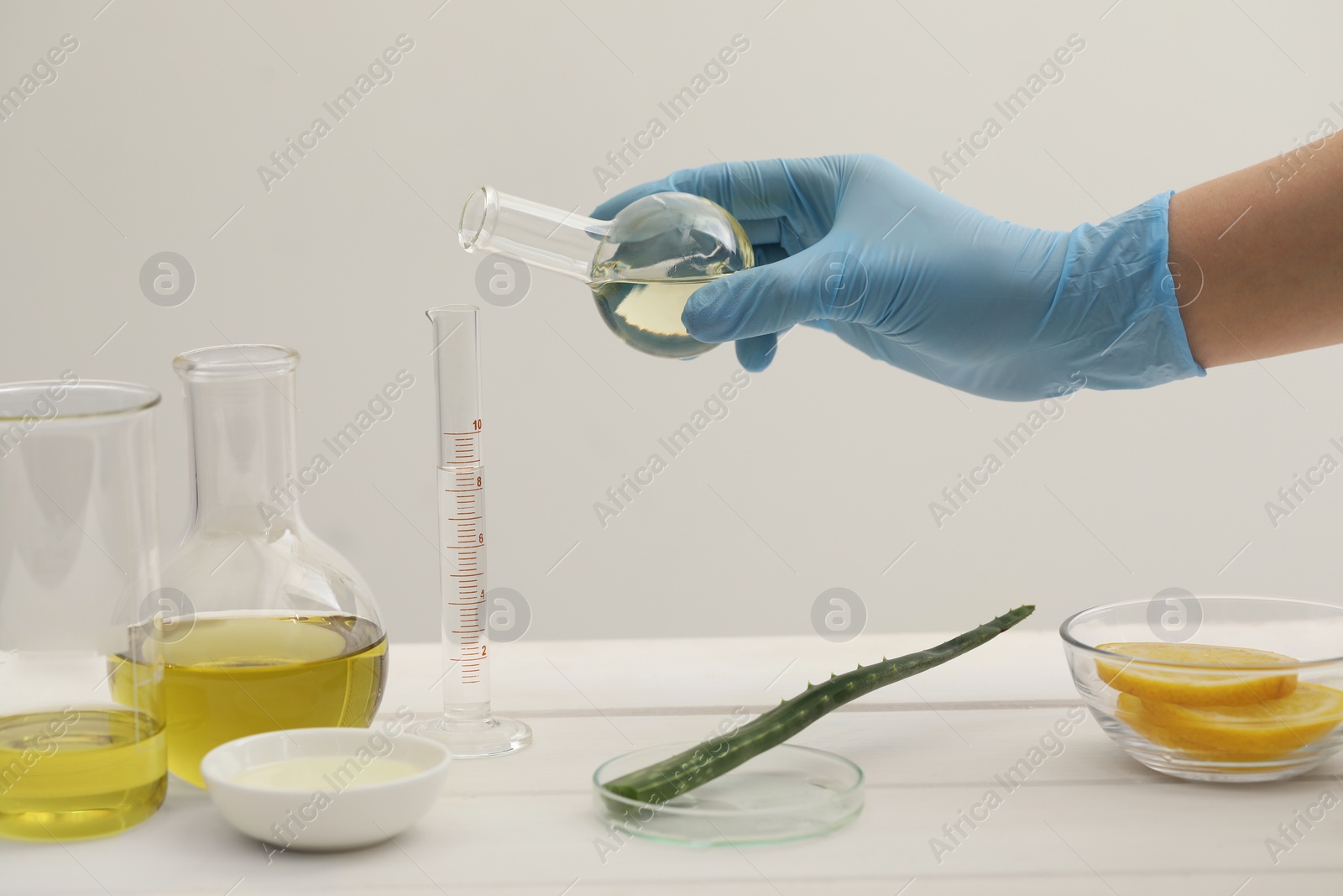 Photo of Scientist developing cosmetic oil at white table, closeup