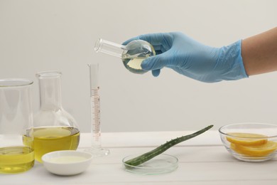 Photo of Scientist developing cosmetic oil at white table, closeup