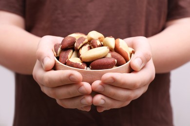 Woman holding bowl with tasty Brazil nuts on blurred background, closeup