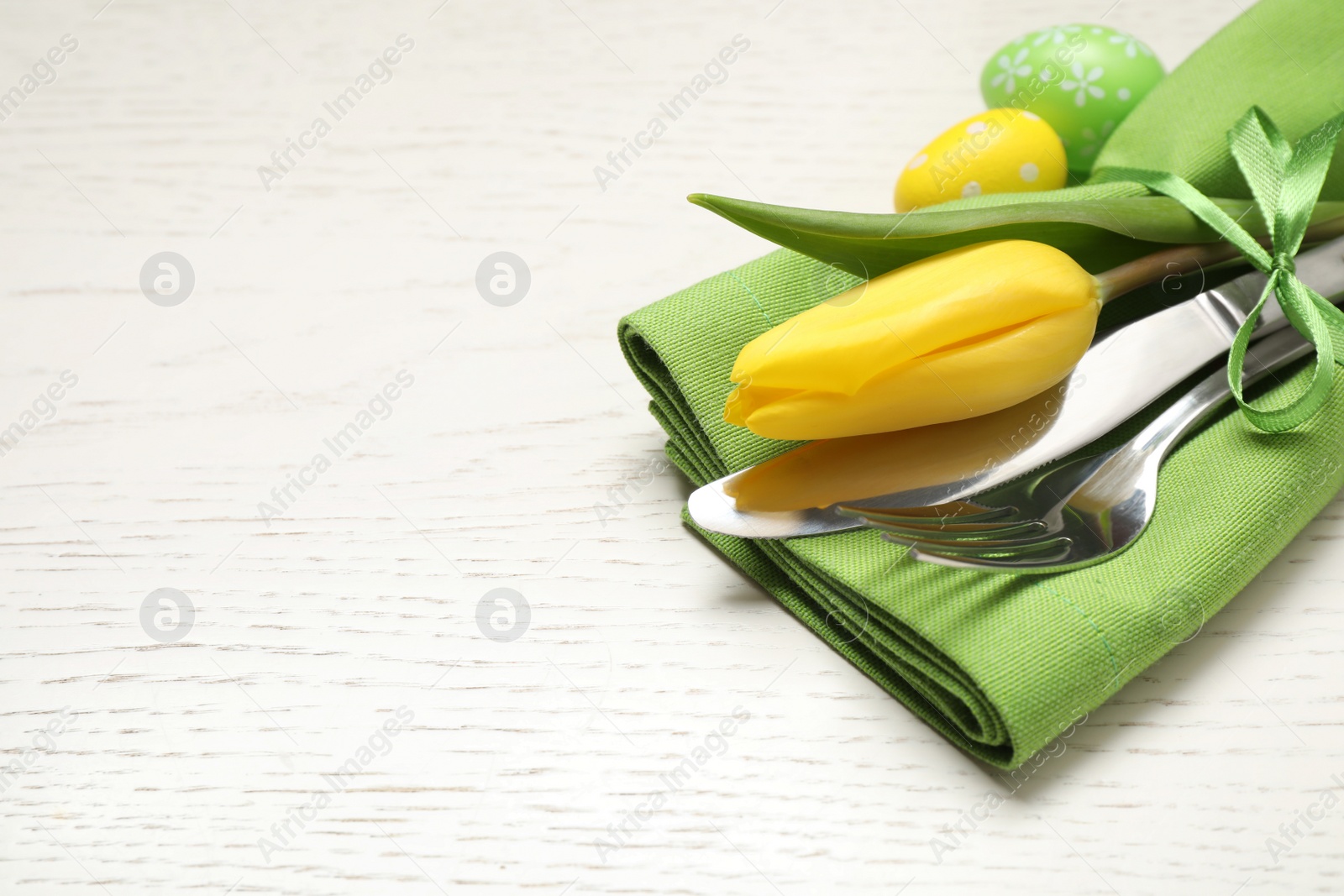 Photo of Cutlery set with beautiful tulip on white wooden table, closeup view with space for text. Easter celebration