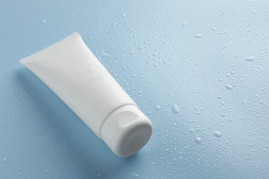 Photo of Moisturizing cream in tube on light blue background with water drops, closeup. Space for text