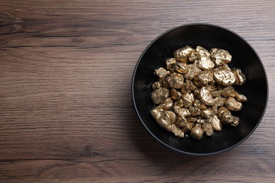 Photo of Bowl of gold nuggets on wooden table, top view. Space for text