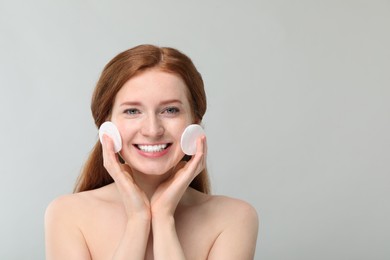 Photo of Smiling woman with freckles wiping face on grey background. Space for text