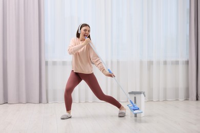 Photo of Enjoying cleaning. Happy woman with mop singing while tidying up at home. Space for text