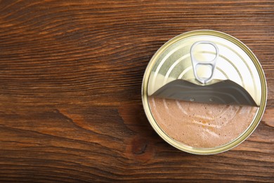 Photo of Open tin can with meat pate on wooden table, top view. Space for text