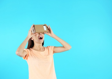 Young woman using cardboard virtual reality headset on color background. Space for text