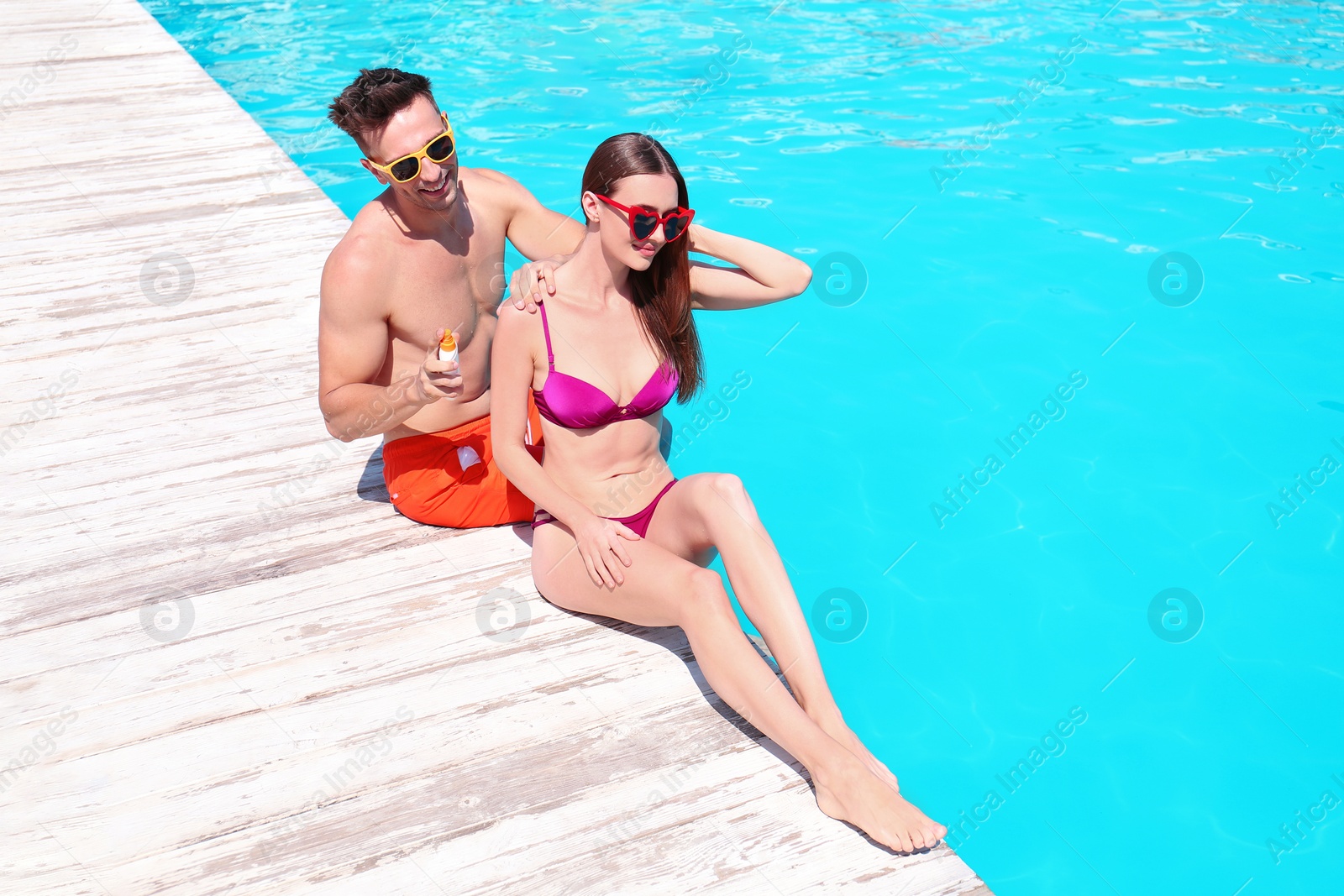 Photo of Young man applying sun protection cream onto girlfriend at swimming pool