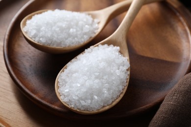 Photo of Organic salt in spoons on wooden plate, closeup