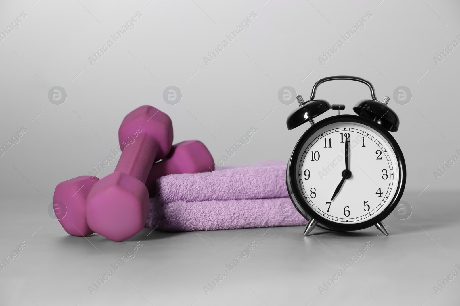 Photo of Alarm clock, towel and dumbbells on grey background. Morning exercise