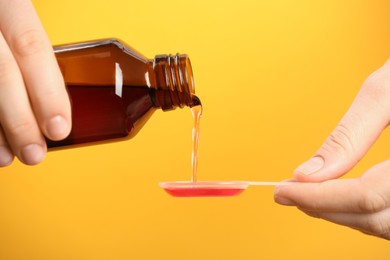 Photo of Woman pouring cough syrup into dosing spoon on orange background, closeup