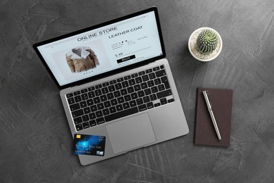 Online store website on laptop screen. Computer, smartphone, stationery, credit card and cactus on grey table, flat lay