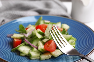 Photo of Delicious fresh cucumber tomato salad and fork on table, closeup