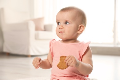 Portrait of cute baby girl with cookie in room