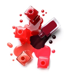 Spilled different nail polishes with bottles on white background, top view