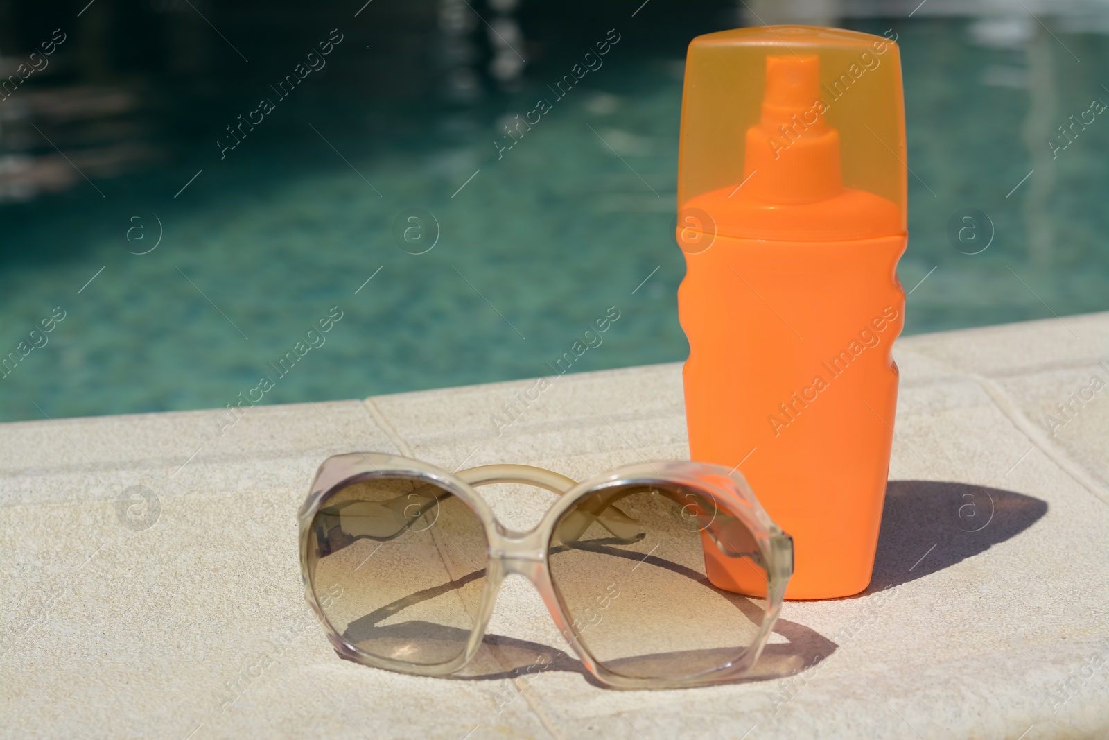 Photo of Stylish sunglasses and sunscreen near outdoor swimming pool on sunny day, space for text. Beach accessories