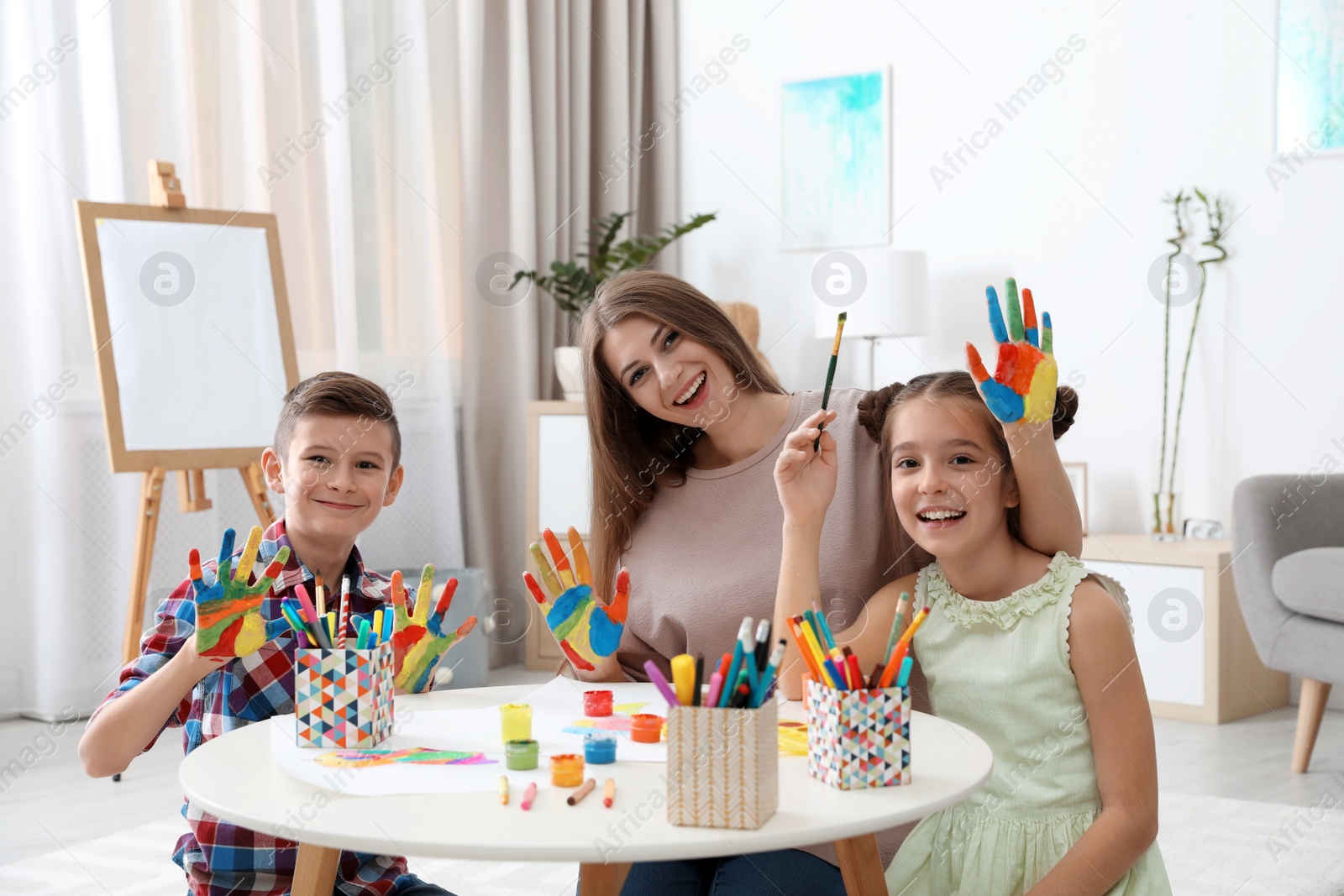 Photo of Cute children and young woman with painted hands at table indoors