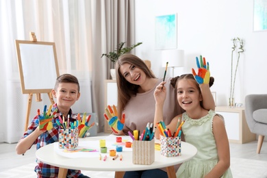 Cute children and young woman with painted hands at table indoors