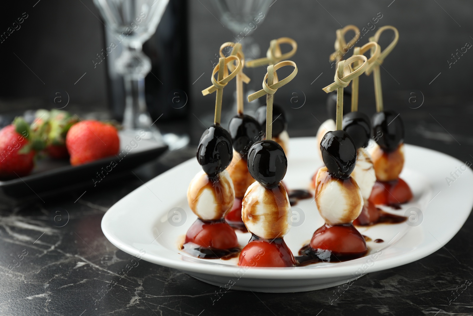 Photo of Tasty canapes with black olives, mozzarella and cherry tomatoes on dark textured table, closeup