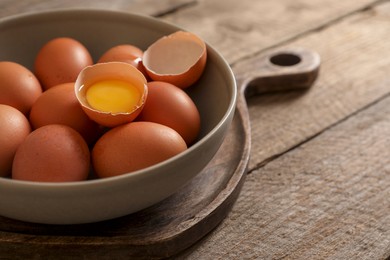 Photo of Bowl with raw chicken eggs on wooden table, closeup. Space for text