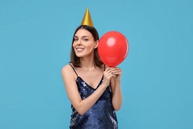 Happy young woman in party hat with balloon on light blue background