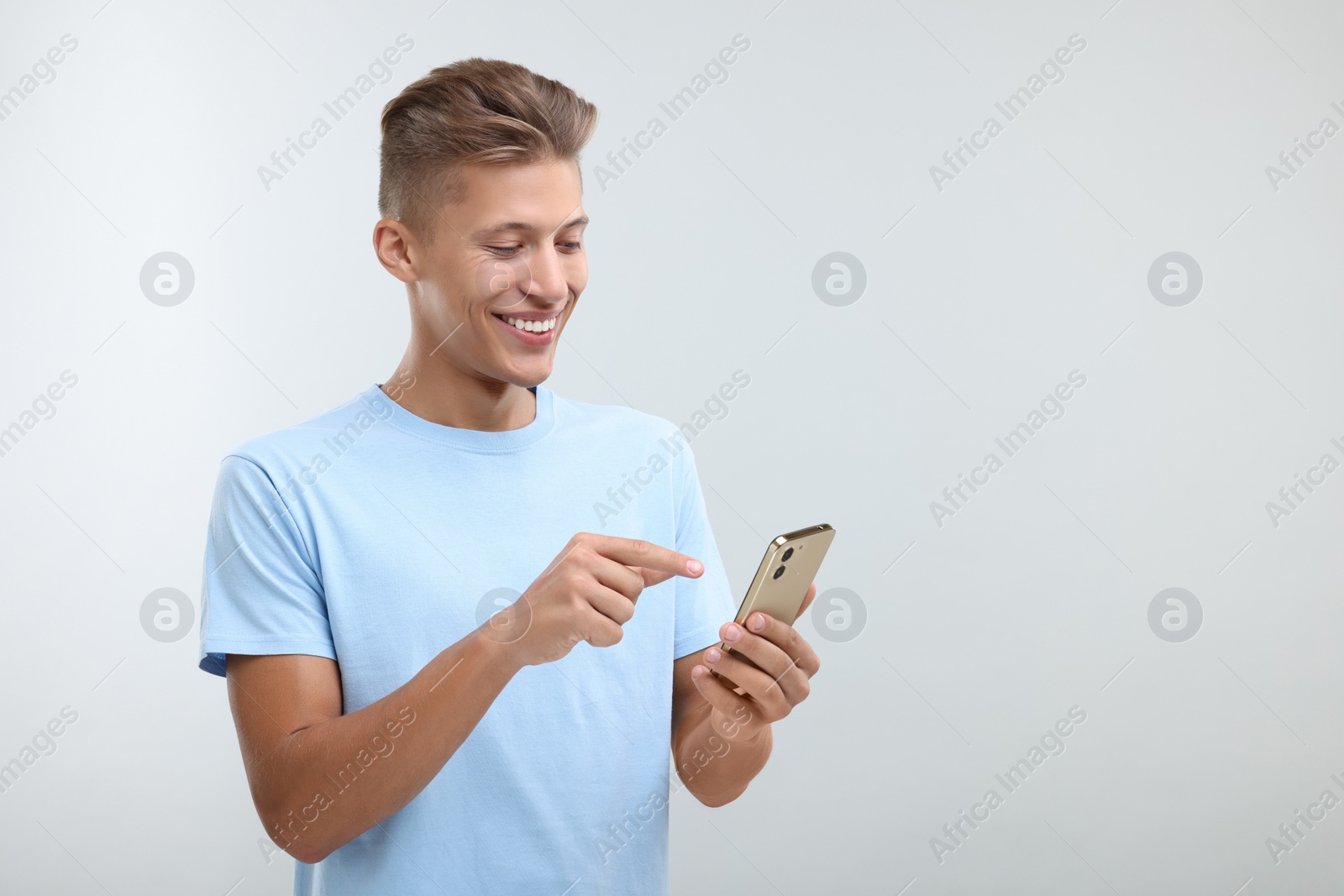 Photo of Happy young man sending message via smartphone on light grey background. Space for text