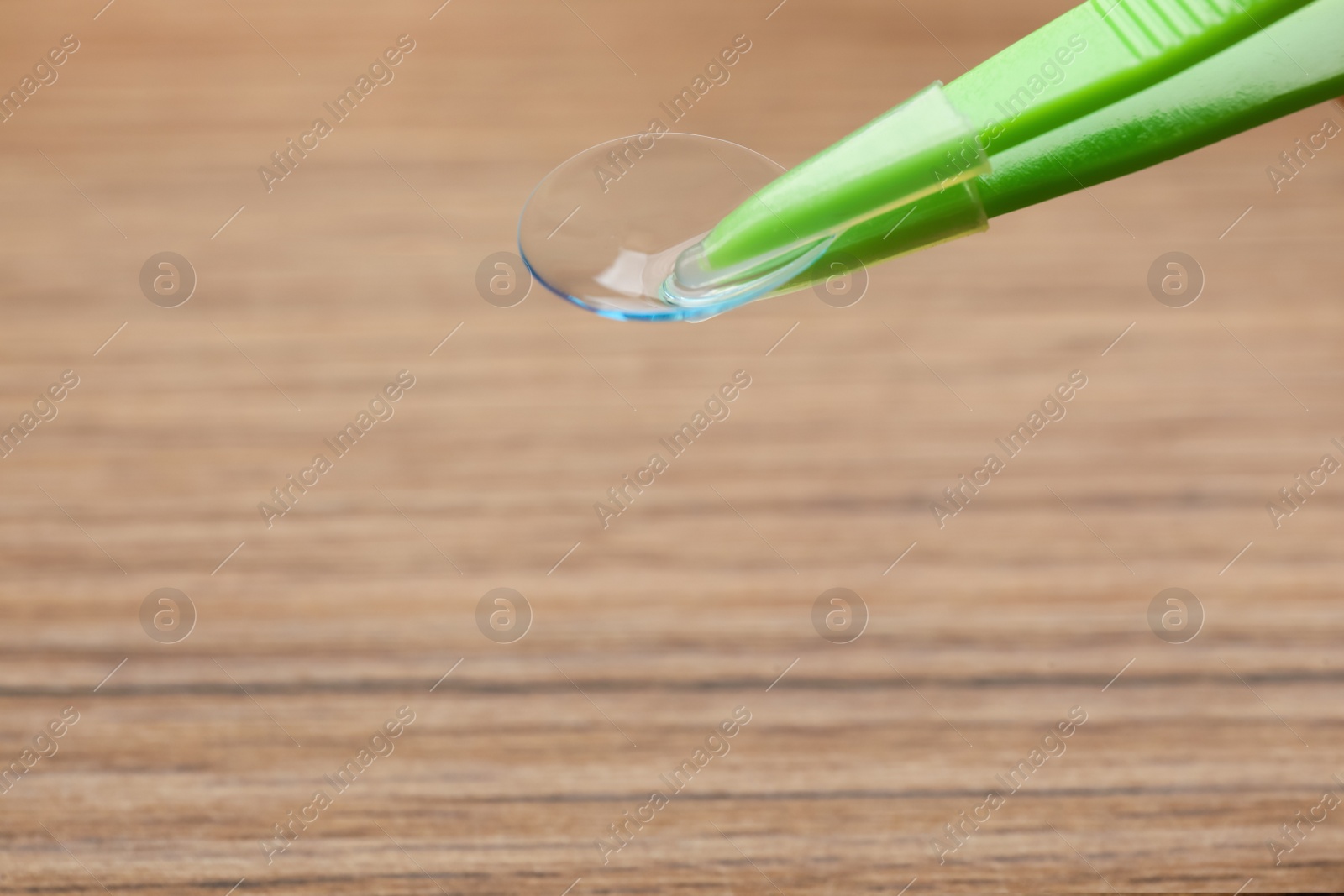 Photo of Tweezers with contact lens on wooden background, closeup. Space for text