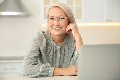 Beautiful mature woman working with laptop in kitchen