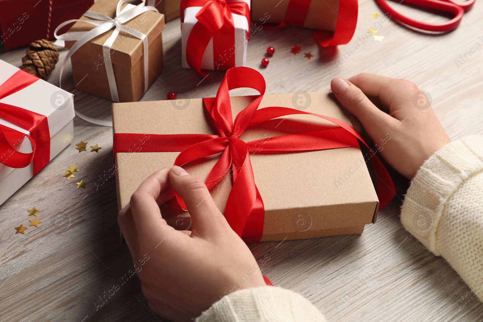 Photo of Woman decorating gift box at white wooden table, closeup. Christmas present