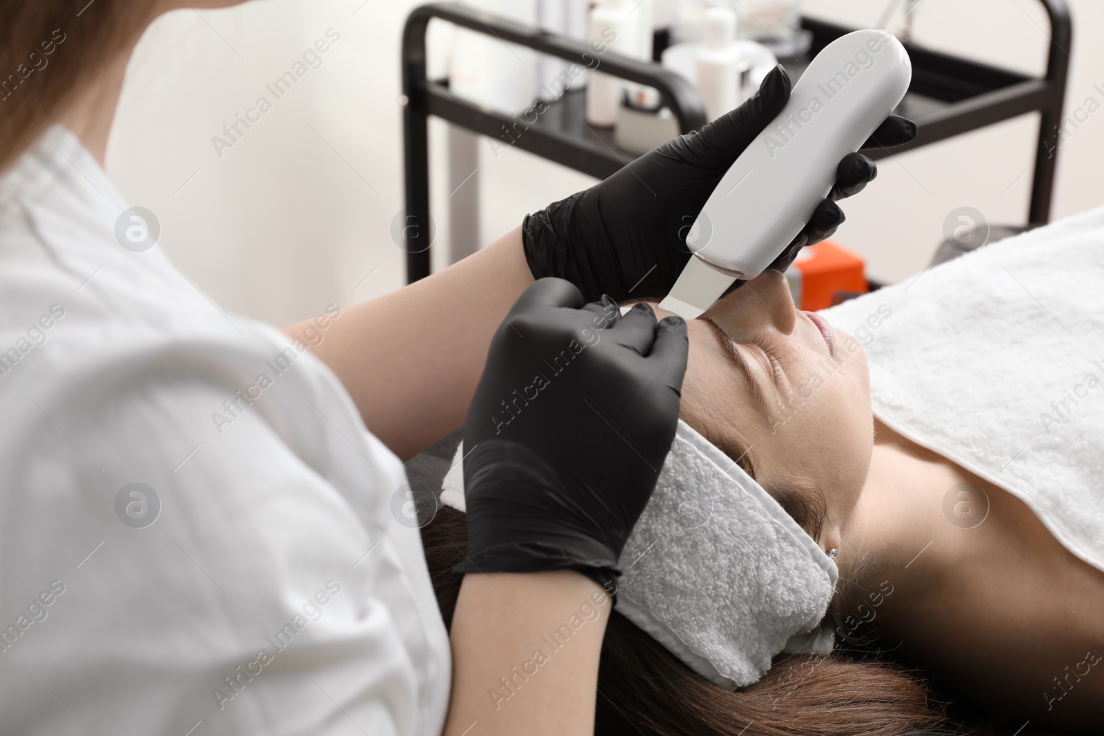 Photo of Cosmetologist using ultrasonic scrubber, closeup. Client having cleansing procedure in clinic