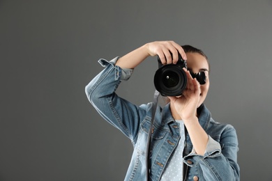 Young woman with camera against gray background. Professional photo studio