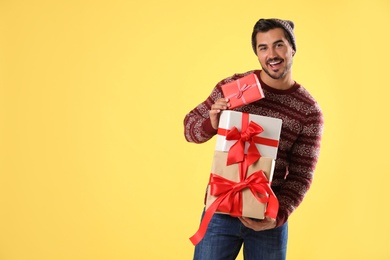 Photo of Happy man in Christmas sweater and hat holding gift boxes on yellow background