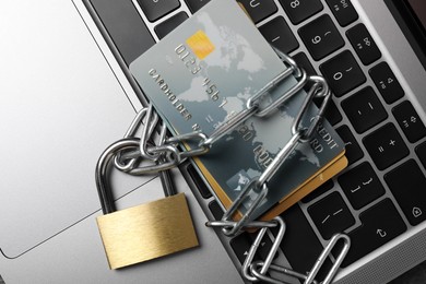 Photo of Cyber security. Metal padlock with chain and credit cards on laptop, top view