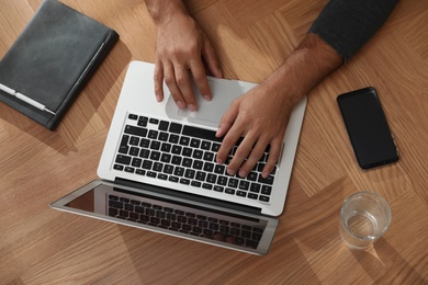 Man using laptop for search at wooden table, top view