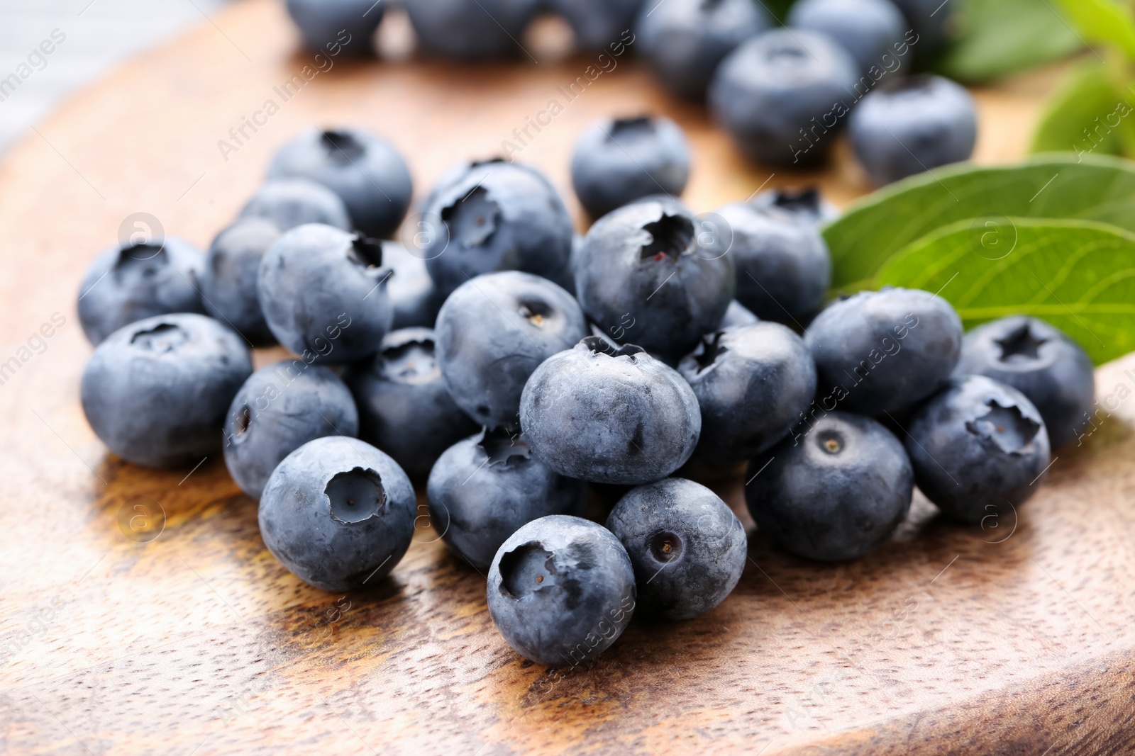 Photo of Tasty fresh blueberries and green leaves on wooden board, closeup