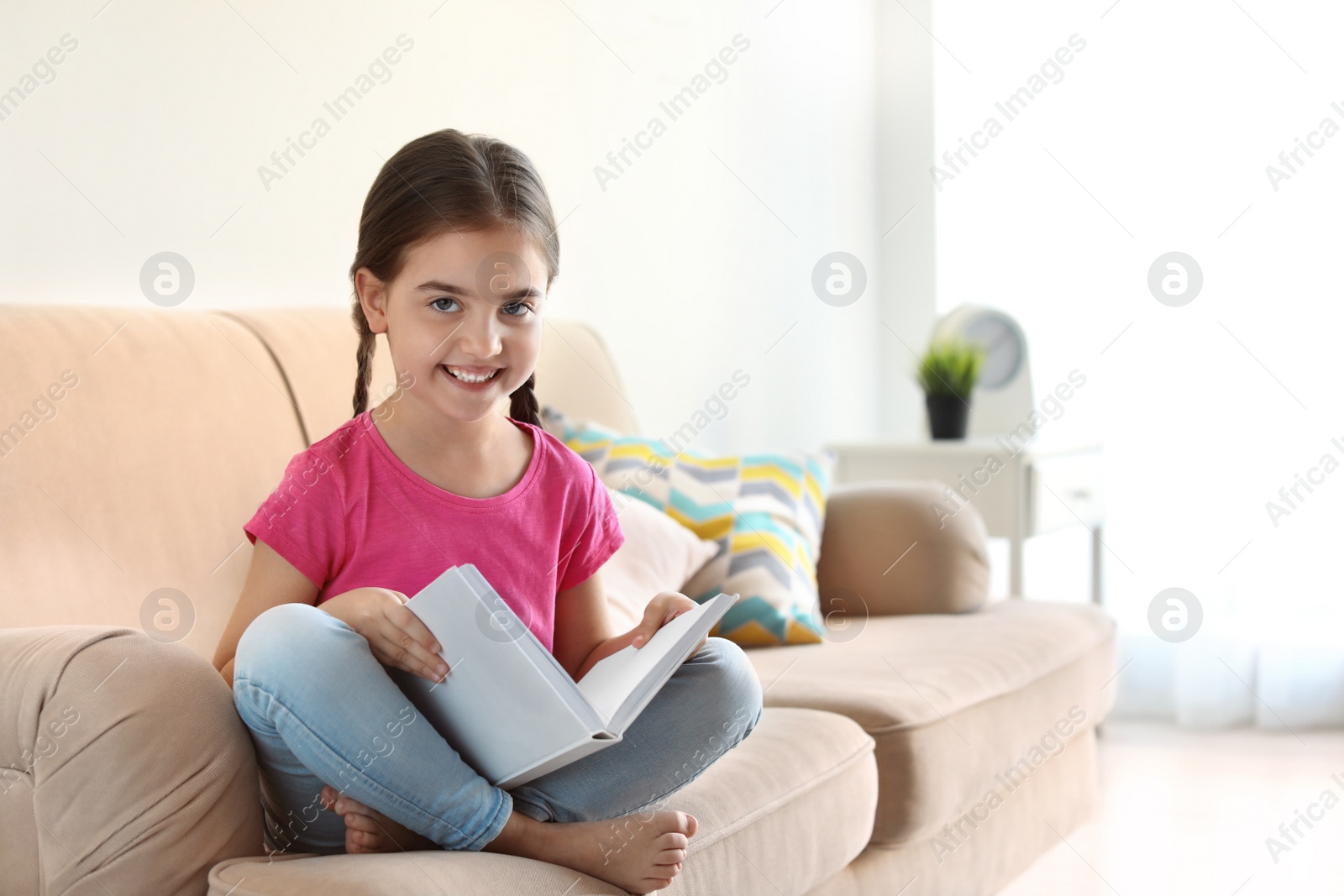 Photo of Cute child reading book on sofa indoors