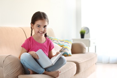 Cute child reading book on sofa indoors