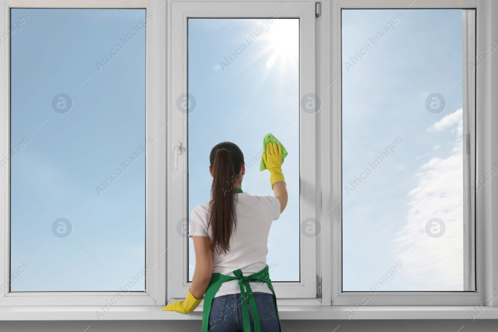 Photo of Woman cleaning window glass with cloth indoors, back view