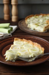 Photo of Plate with piece of tasty leek pie and fork on wooden table, closeup