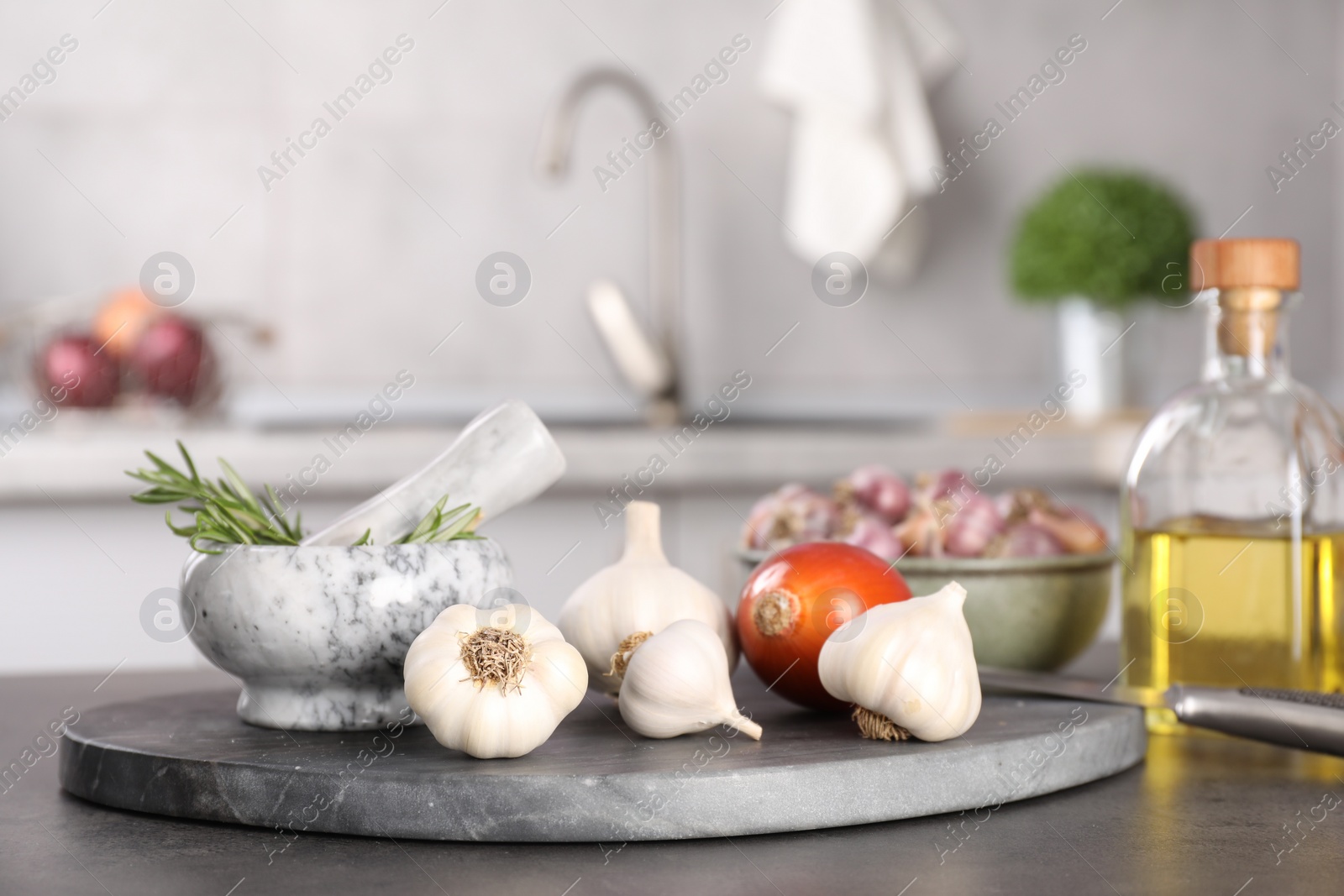 Photo of Fresh raw garlic, onion, rosemary and oil on grey table