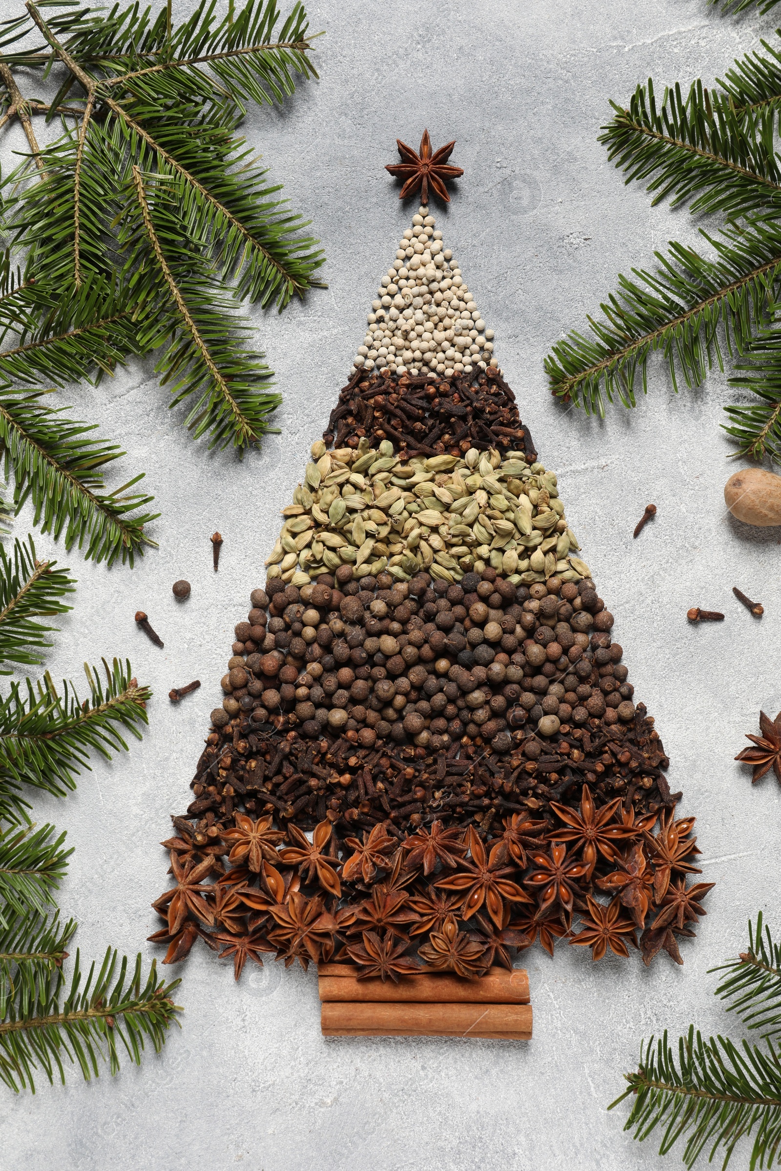 Photo of Christmas tree made of different spices and fir branches on gray textured table, flat lay