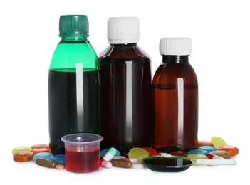 Photo of Bottles of cough syrup, dosing spoon, measuring cup and pills on white background