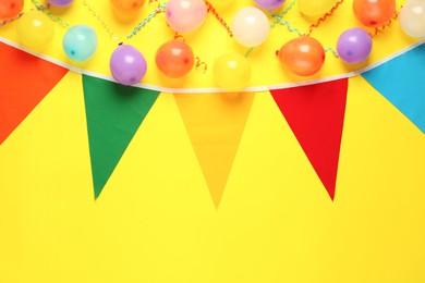 Bunting with colorful triangular flags and other festive decor on yellow background, flat lay