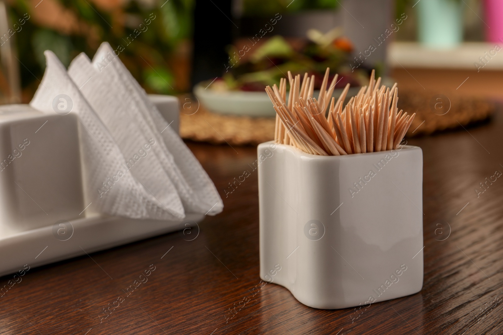 Photo of Holder with many toothpicks on wooden table, closeup. Space for text